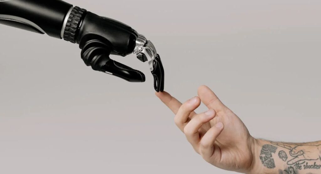 A snapshot of a tattooed human hand reaching out and touching the fingers of a robotic arm